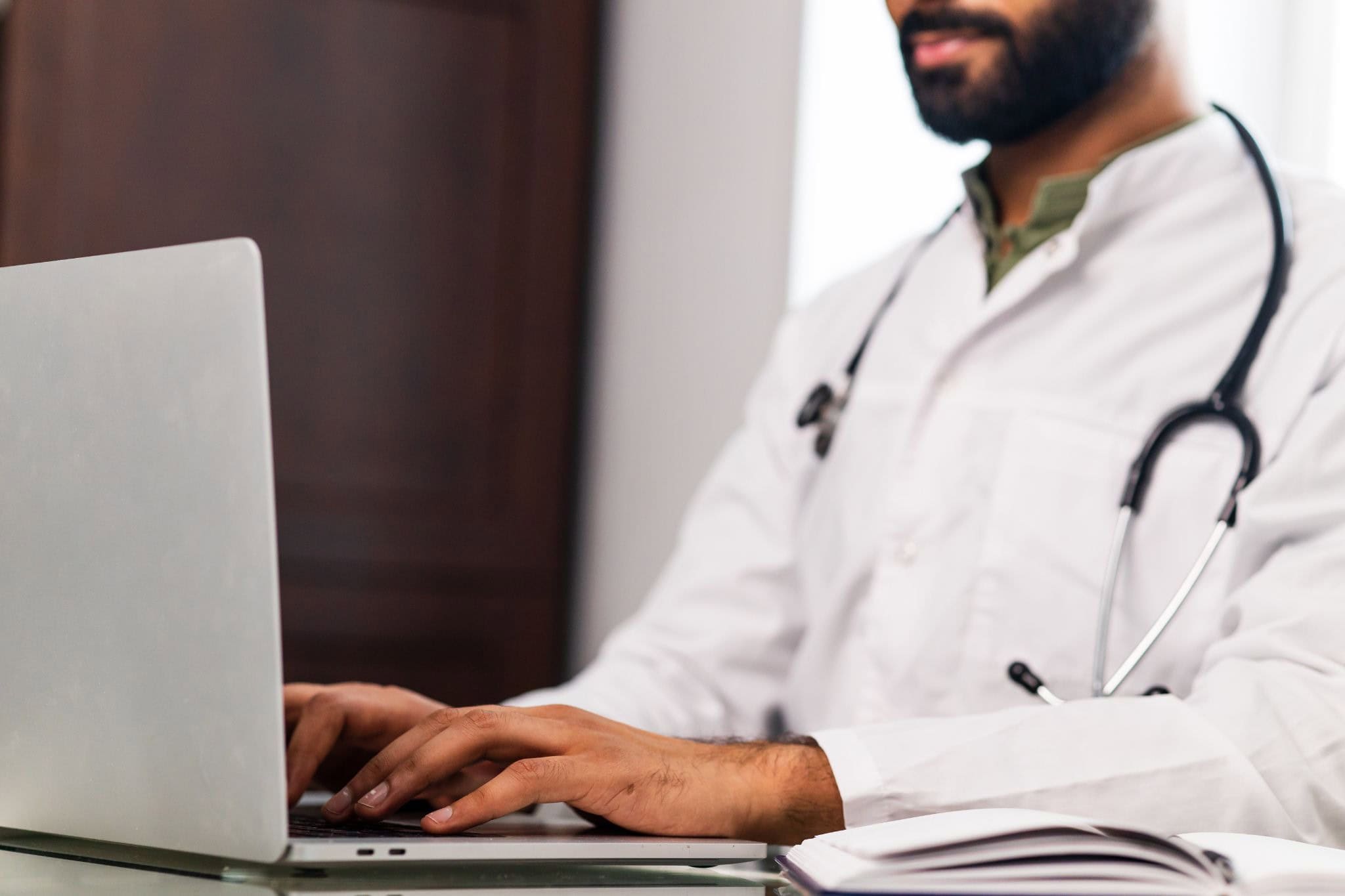 Médico con estetoscopio consultando contenido de formación médica continuada en su portátil